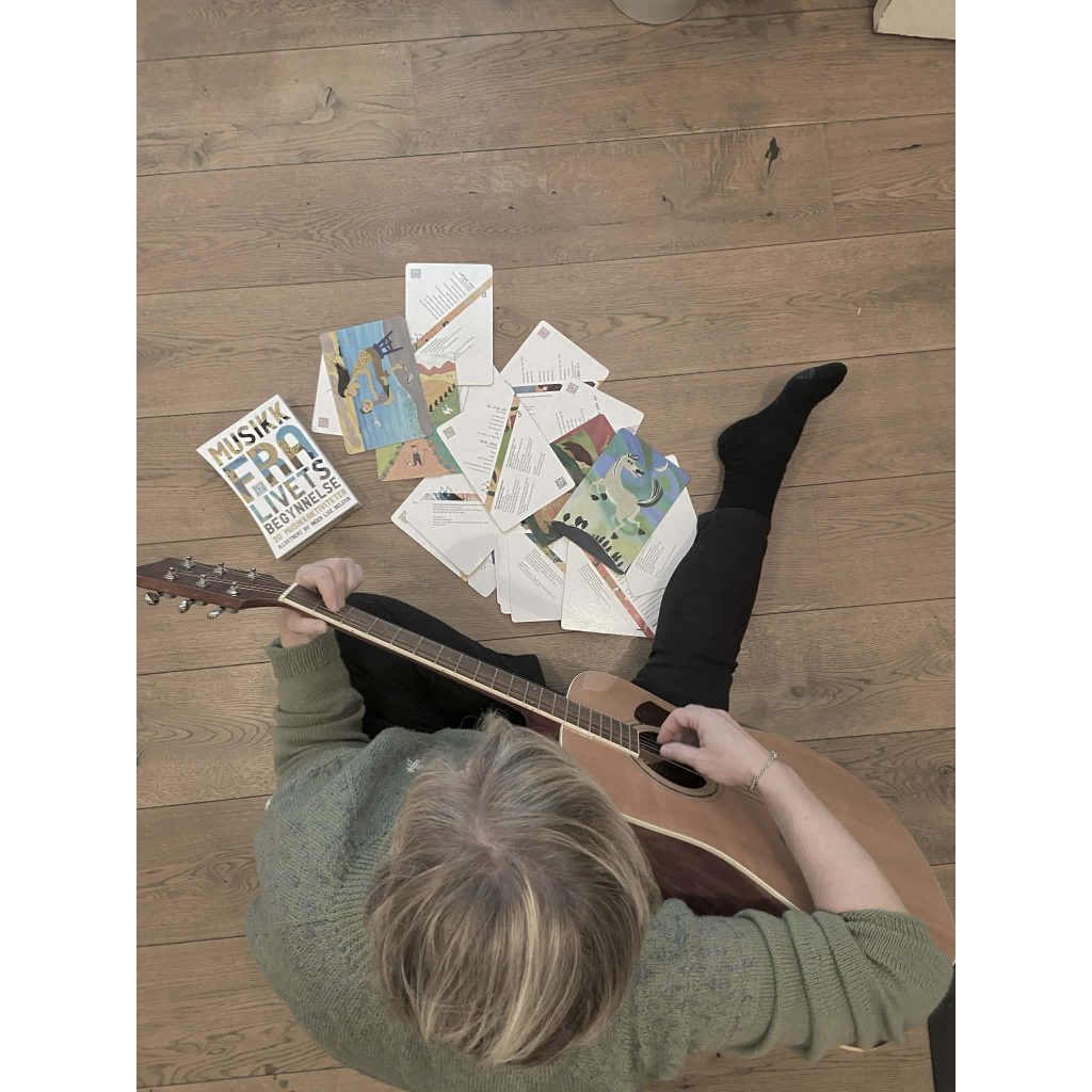Bildet er tatt ovenfra og ser Ingrid som spiller gitar, med bøker foran seg