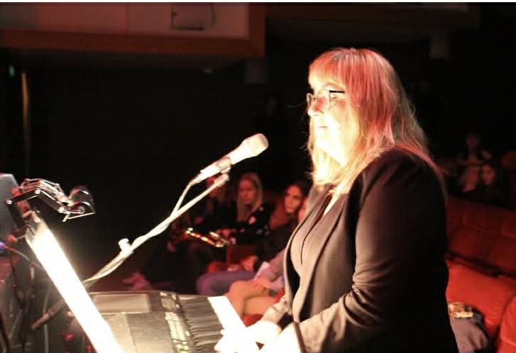 sideprofil av Ingrid som spiller piano, det er rødt scene lys i bildet