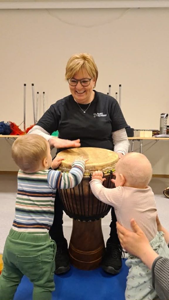 Ingrid som spiller to trommer med to små barn 